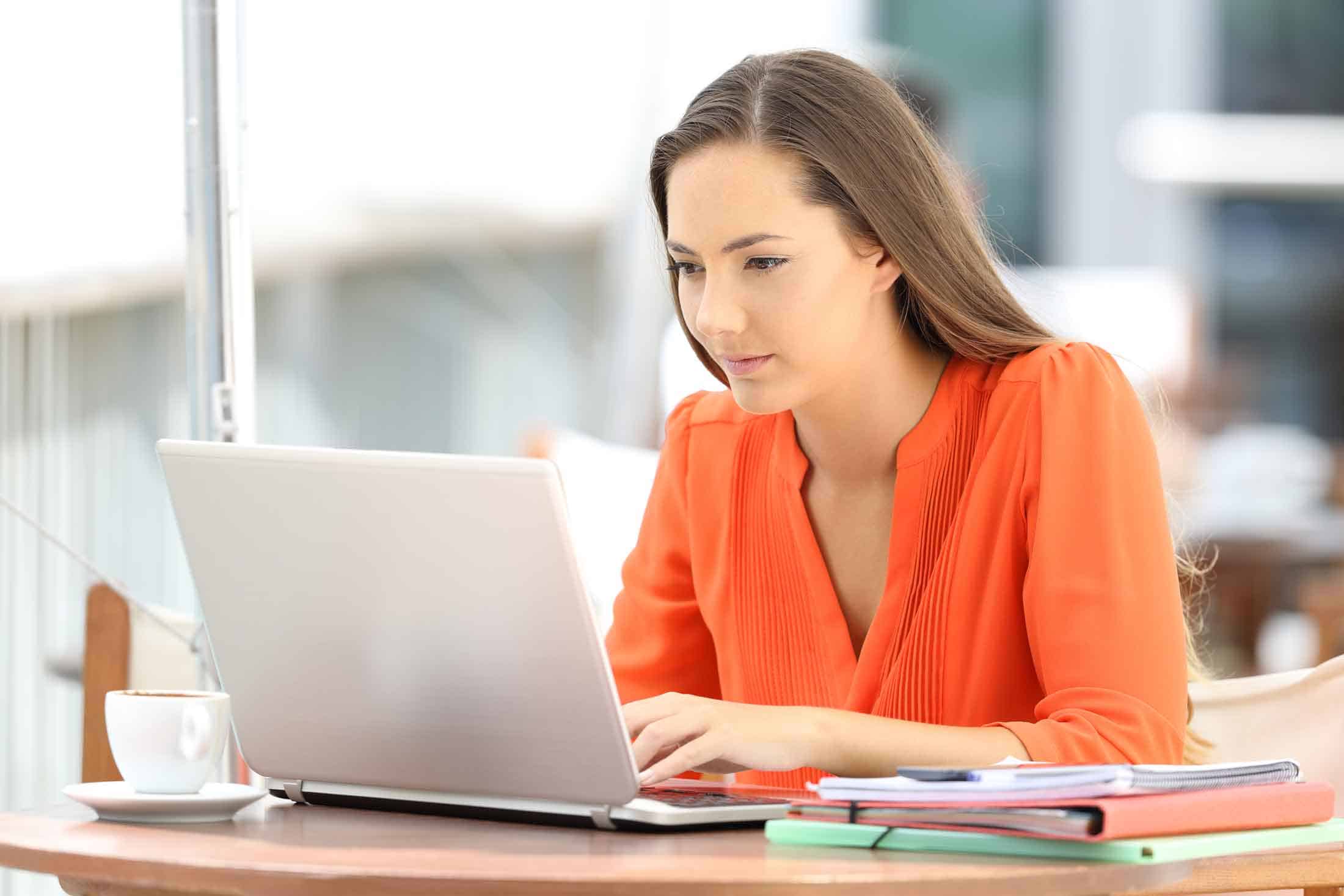 Woman in an orange shirt working on a laptop
